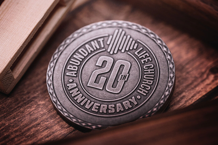 Antique silver challenge coin marking a church's 20th anniversary on a wooden table