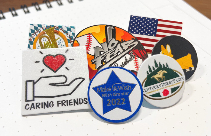 Assortment of custom lapel pins in flag, sports and charity designs on a notebook